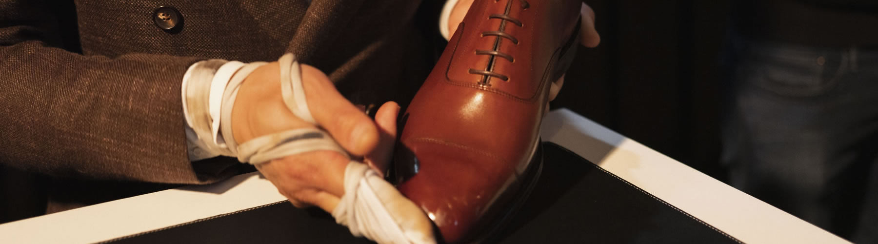 A shoemaker's bandaged hand holds a polished brown leather shoe, hinting at the craft and care behind quality footwear.