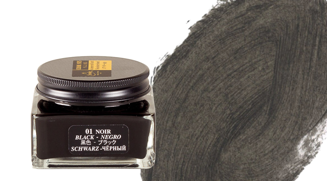 A glass jar of black ink labeled in multiple languages sits next to a textured brushstroke of black ink on a white background.
