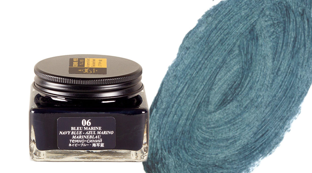 A glass jar of navy blue ink labeled Bleu Marine 06 sits next to a textured navy blue ink swatch painted in a circular pattern.