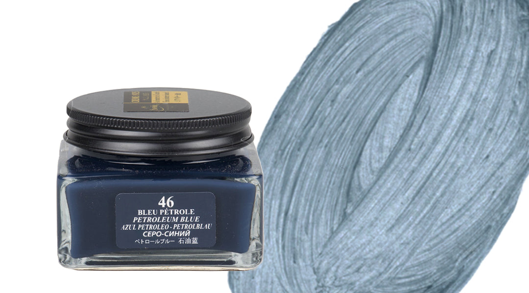 A square glass jar of petroleum blue paint labeled “46 BLEU PETROLE PETROLEUM BLUE” sits next to a textured swatch of the same blue color, shown in thick, swirling brushstrokes.