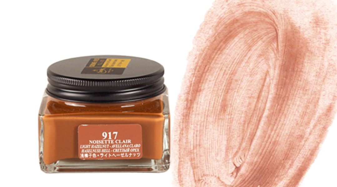 A glass jar labeled “917 Noisette Clair” with a brown lid, filled with light hazelnut-colored ink, sits beside a thick, swirling brushstroke of the ink in a soft, brownish-pink shade.